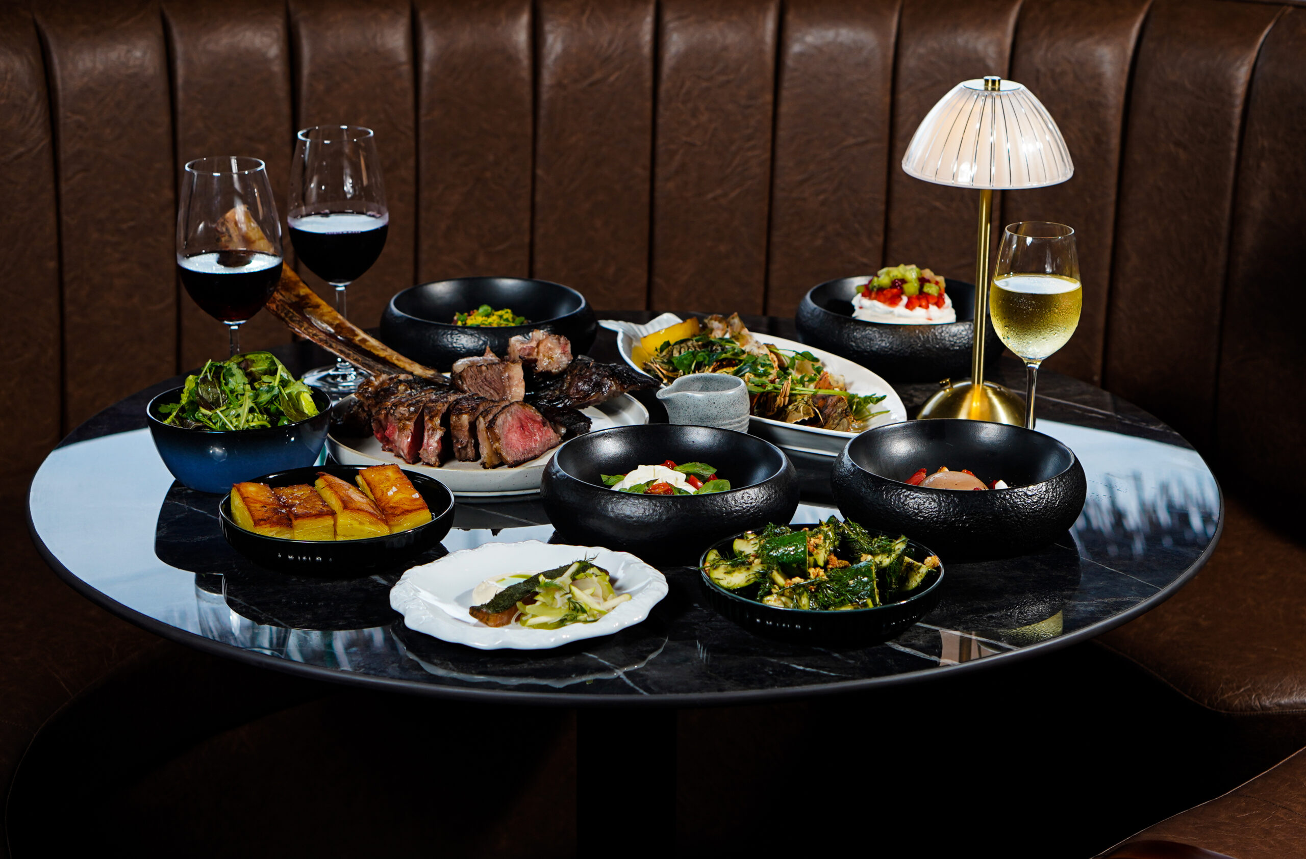 A spread of food from a steakhouse inlcuding vegetables, steaks and seafood